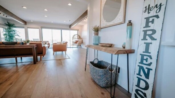A spacious living area with a wooden floor, a sofa, a coffee table, and a wall-mounted sign that reads "Hey FRIENDS". - Vibey😎Pool House🏡 ModernFarmhouse 1700sqft + View🌄 (Lakeside)