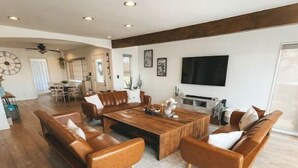 A spacious living room with a large wooden coffee table, leather sofas, and a dining area in the background. - Vibey😎Pool House🏡 ModernFarmhouse 1700sqft + View🌄 (Lakeside)