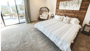 A bedroom with a large bed, a wooden headboard, a view of the outdoors, and a chair by the window. - Vibey😎Pool House🏡 ModernFarmhouse 1700sqft + View🌄 (Lakeside)