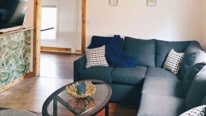 Ett vardagsrum med en mörkgrön soffa, två hängande taklampor, ett soffbord i glas och en synlig takbalk i trä.