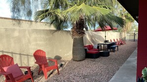 An outdoor seating area with red chairs and a table, surrounded by gravel and palm trees. - Urban escape,Next to shopping center and restaurants! (Phoenix)