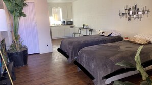 A bedroom with two beds, a potted plant, a desk, and a kitchenette in the background. - Urban escape,Next to shopping center and restaurants! (Phoenix)