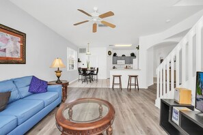 Un salon avec un canapé bleu, une table basse en bois et un ventilateur de plafond.