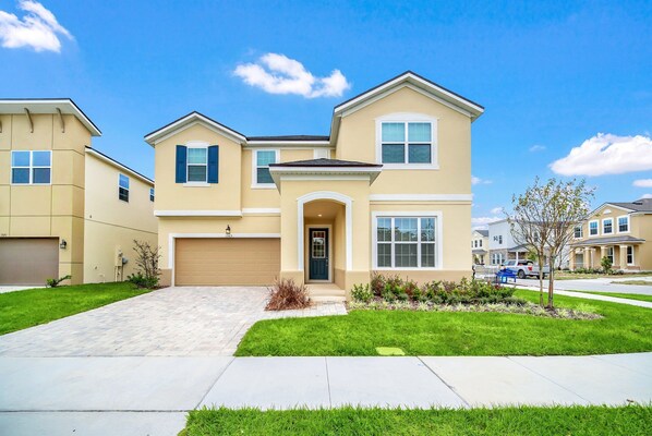 A two-story residential house with a front garage, a well-maintained lawn, and a clear blue sky.