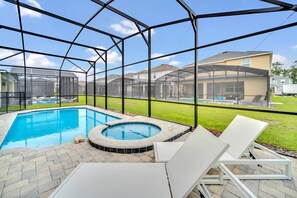 A backyard with a swimming pool, hot tub, and lounge chairs.