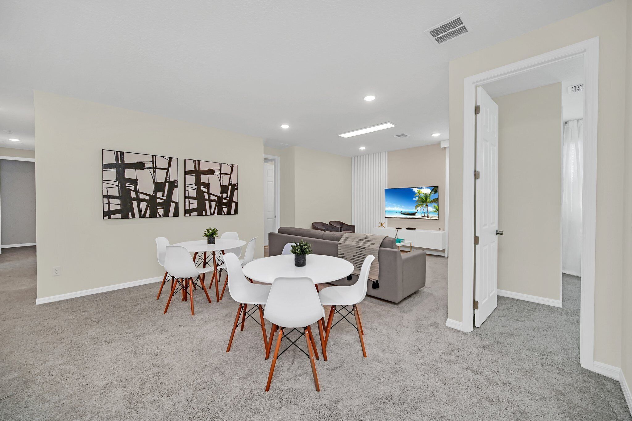 A modern living room with a dining area, a gray sofa, and a flat-screen TV.