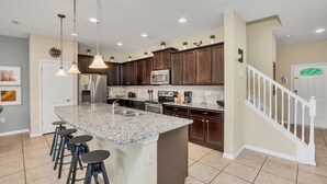 Una cocina con encimeras de granito, electrodomésticos de acero inoxidable y una isla central con taburetes de bar.