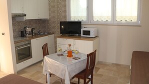 A compact kitchen with white cabinets, a microwave, a television, and a dining table with chairs.