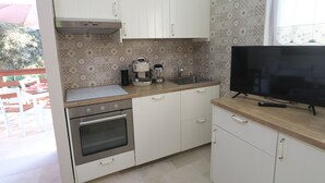 A kitchen with white cabinets, a stove, a coffee maker, and a TV on the counter.