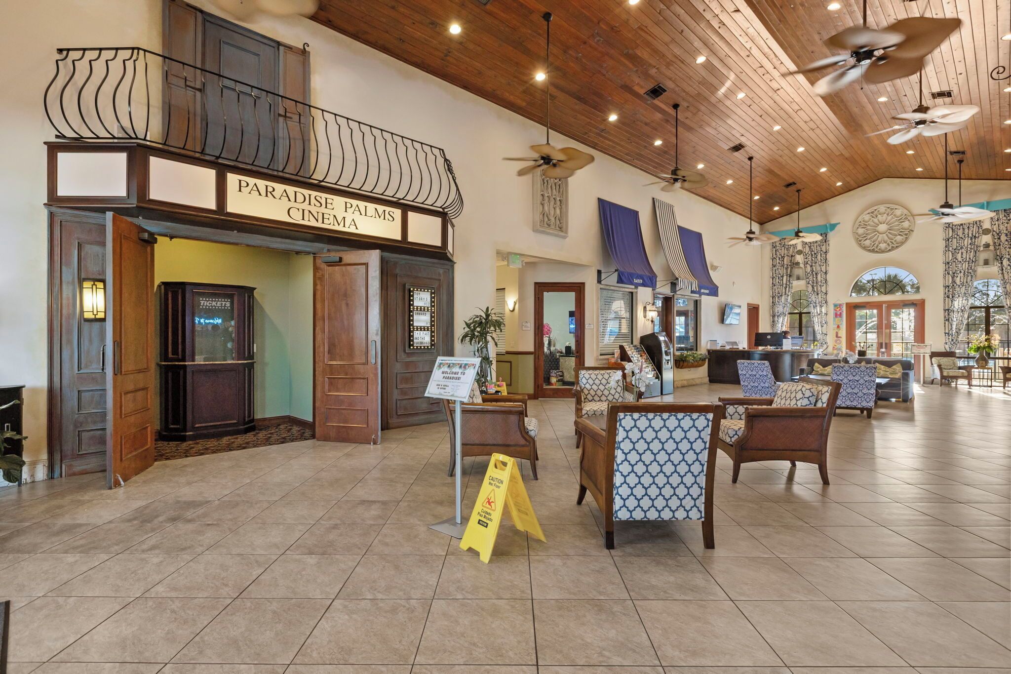 A cinema with a sign reading 'Paradise Palms Cinema' and a reception area with seating and a sign that says 'Welcome to Paradise Palms.'