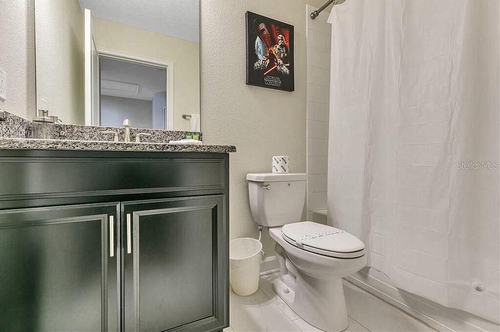 A bathroom with a white toilet, dark cabinets, a granite countertop, and a Star Wars poster on the wall.