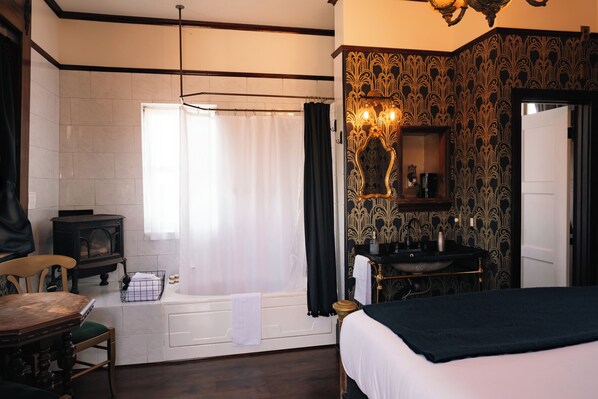 A room with a bed, a wooden table, a chair, a bathtub, a sink, and a mirror.