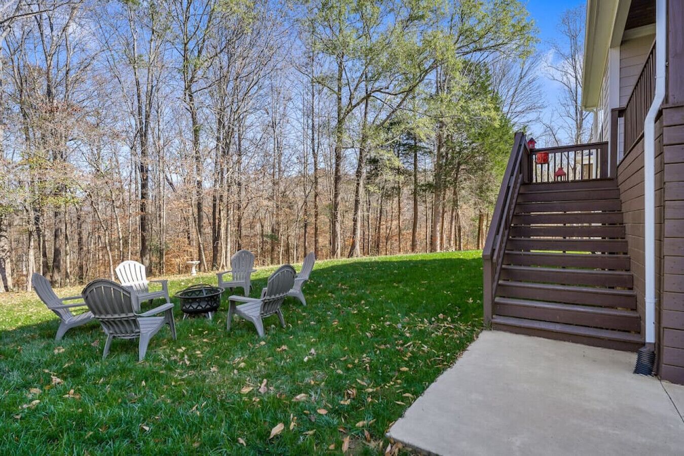 A backyard with a wooden staircase leading to a house, a fire pit, and Adirondack chairs.