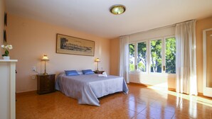 A bedroom with a bed, two bedside tables, a nightstand, a painting, and a window with curtains.