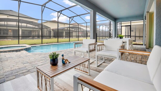 Un patio couvert avec une piscine, du mobilier d’extérieur et une vue sur une maison, le tout protégé par une moustiquaire.