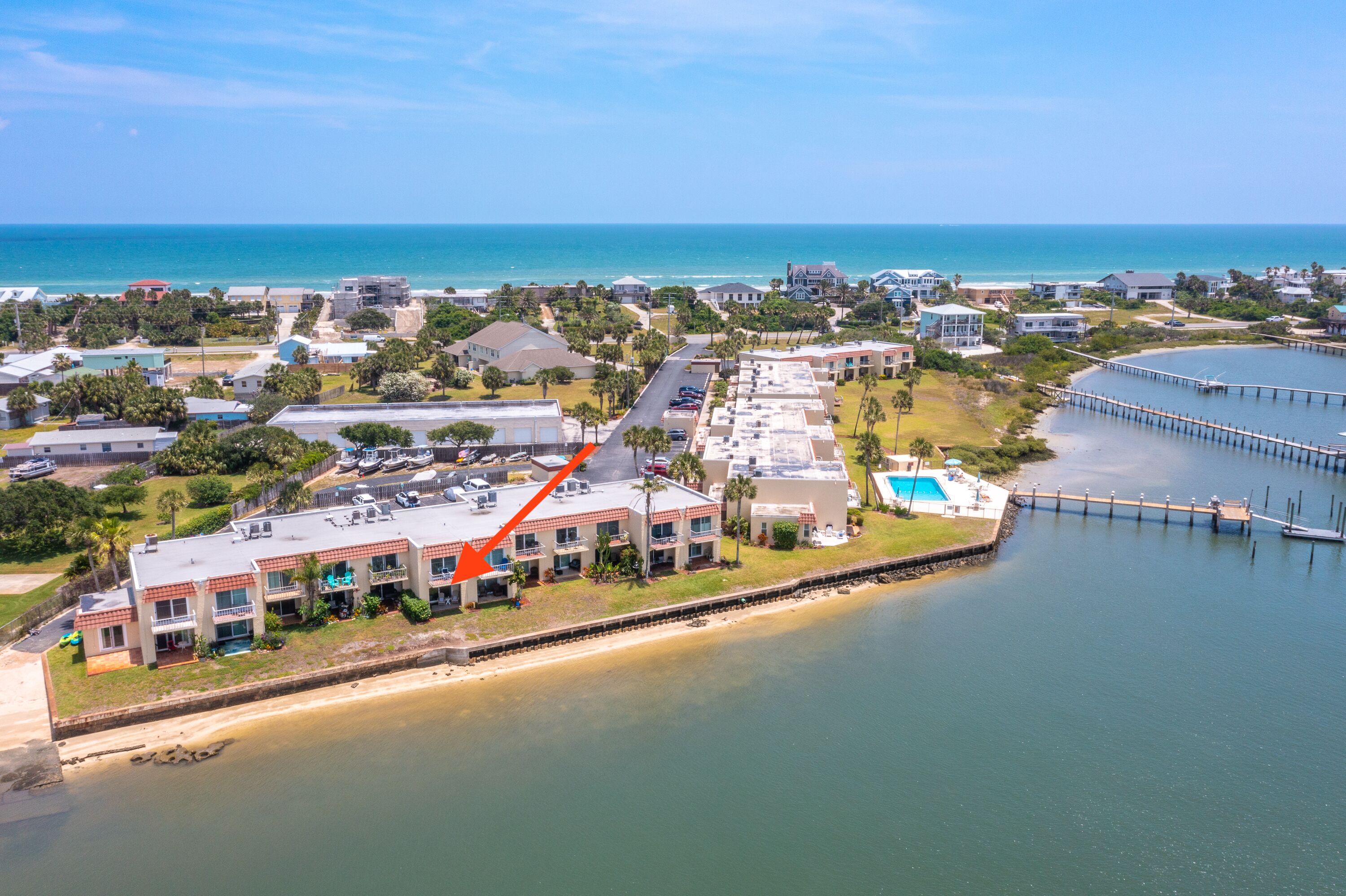 An aerial view of a coastal area with a large building complex, a pier, and a beach.