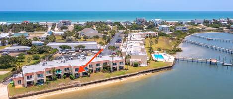 An aerial view of a coastal area with a large building complex, a pier, and a beach.