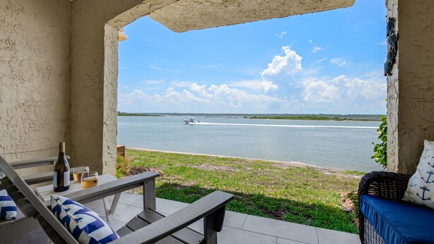 Eine Terrasse mit Blick auf einen See, ein Boot und eine Weinflasche auf einem Tisch.