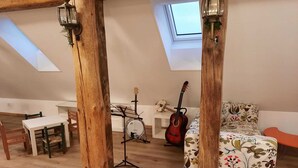 Une pièce de style loft avec des poutres en bois apparentes, une lucarne, un support pour banjo, une guitare, une table blanche avec des chaises et un canapé à motifs floraux.