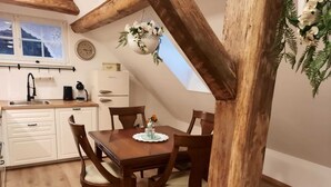 Un coin repas chaleureux avec une table et des chaises en bois, un réfrigérateur blanc, un évier et une fenêtre ornée de rideaux en dentelle.