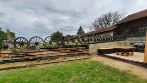Un espace extérieur rustique agrémenté d’un banc en bois, d’un barbecue et d’une structure décorative en forme de roue.