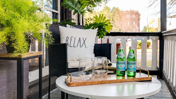 Et rundt bord med en bakke, der indeholder to glas og to Pellegrino vandflasker, en pude med teksten 'RELAX' og en potteplante.