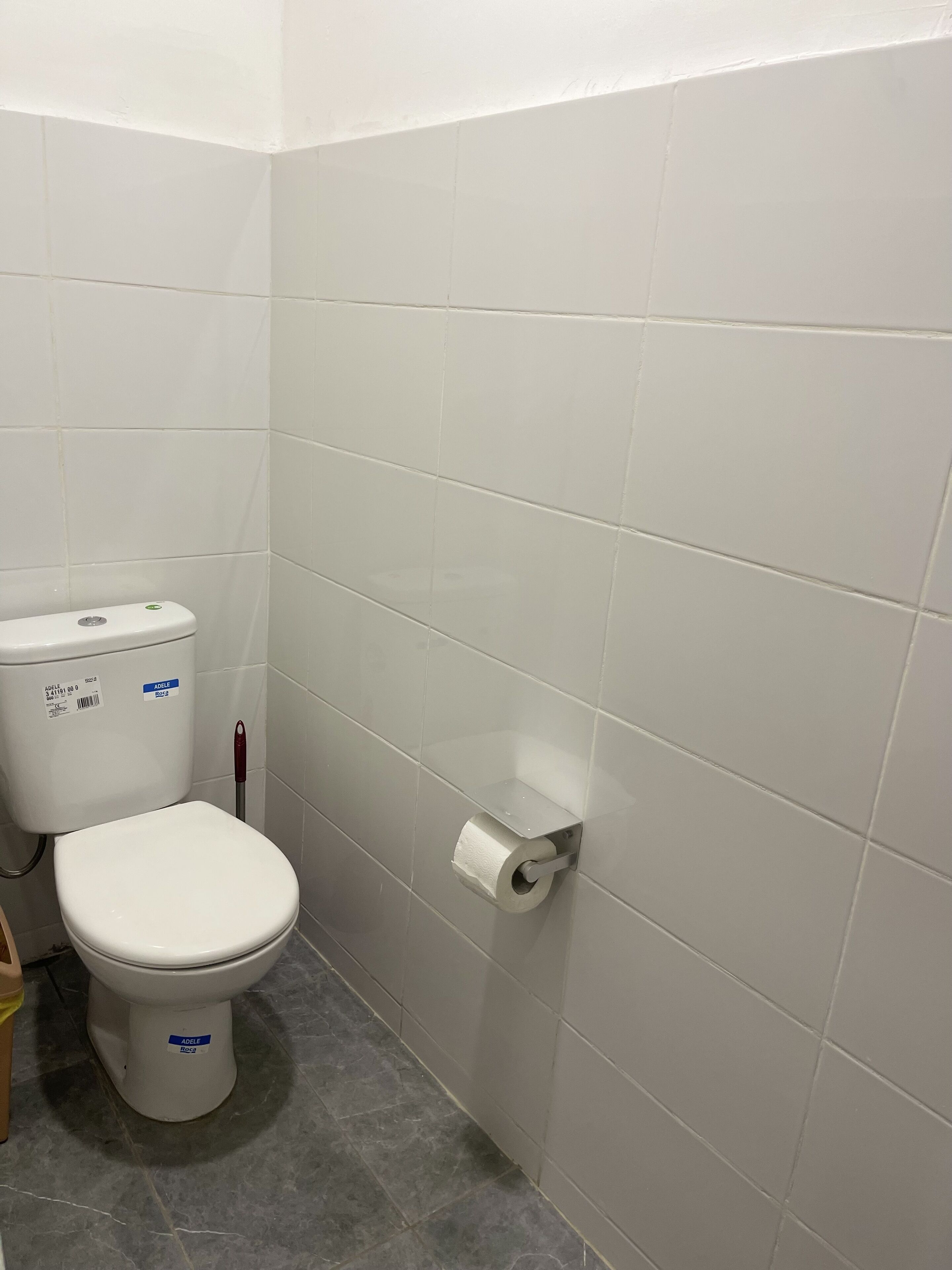 Un baño pequeño y limpio con azulejos blancos, un inodoro y un dispensador de papel higiénico.