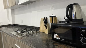 A kitchen with a gas stove, a black microwave, and a kettle on the counter. - AMERICAN MALL (Accra)