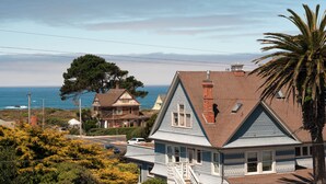 A coastal house with a prominent view of the ocean, a large tree, and a clear sky.