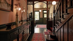 A hallway with a wooden staircase, a red patterned rug, and a framed picture on the wall.