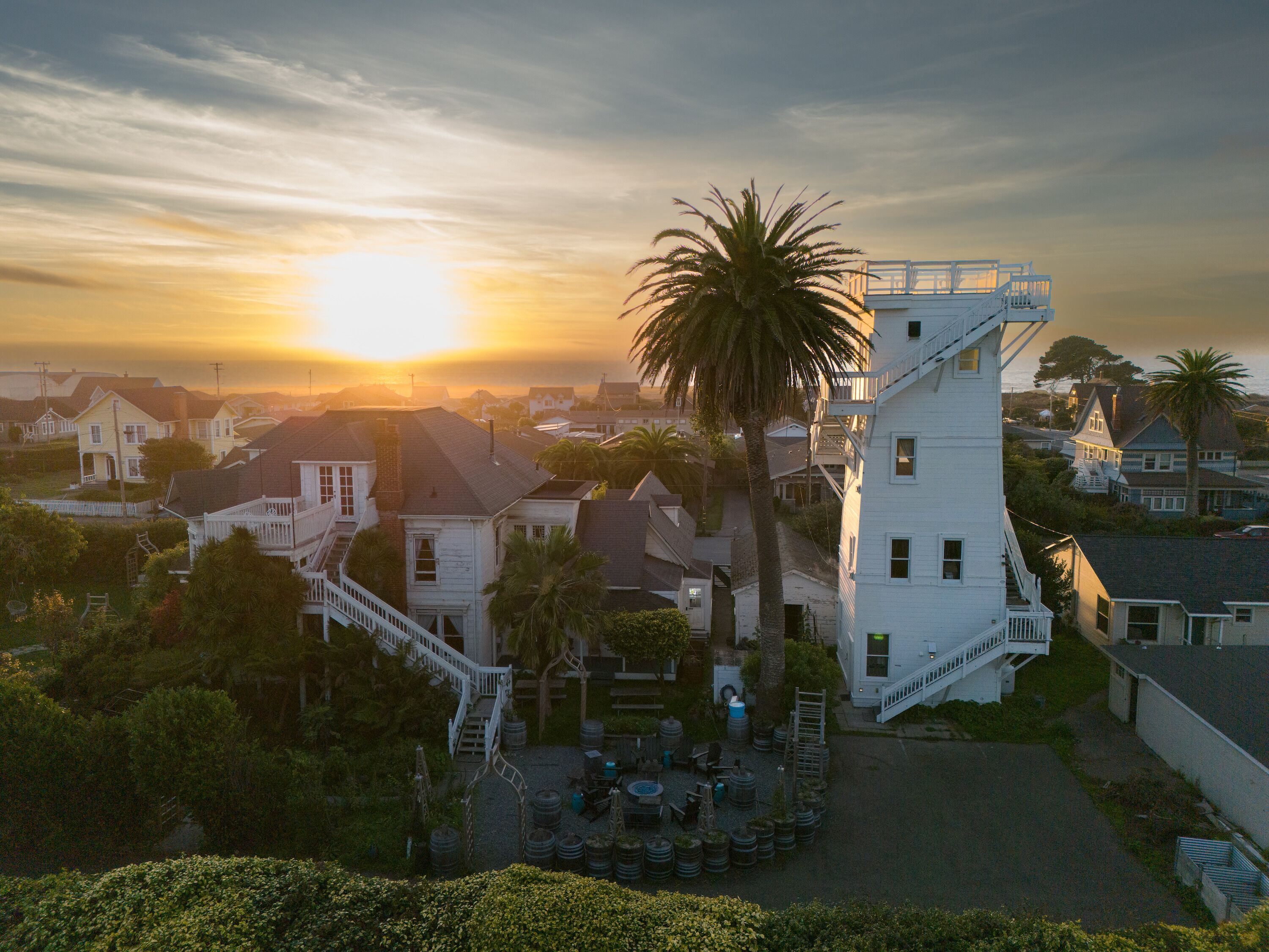 A residential area with houses, a prominent white building with a staircase, and a palm tree.