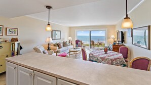 A spacious living area with a kitchen, dining table, and seating. A large window offers a view of the ocean. - Direct Oceanfront Condo on S. Hutchinson Island/Stuart (Stuart)