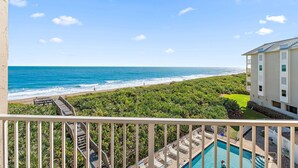 A balcony with a view of a beach and ocean, a pool area with lounge chairs, and a building with a flat roof and multiple windows. - Direct Oceanfront Condo on S. Hutchinson Island/Stuart (Stuart)