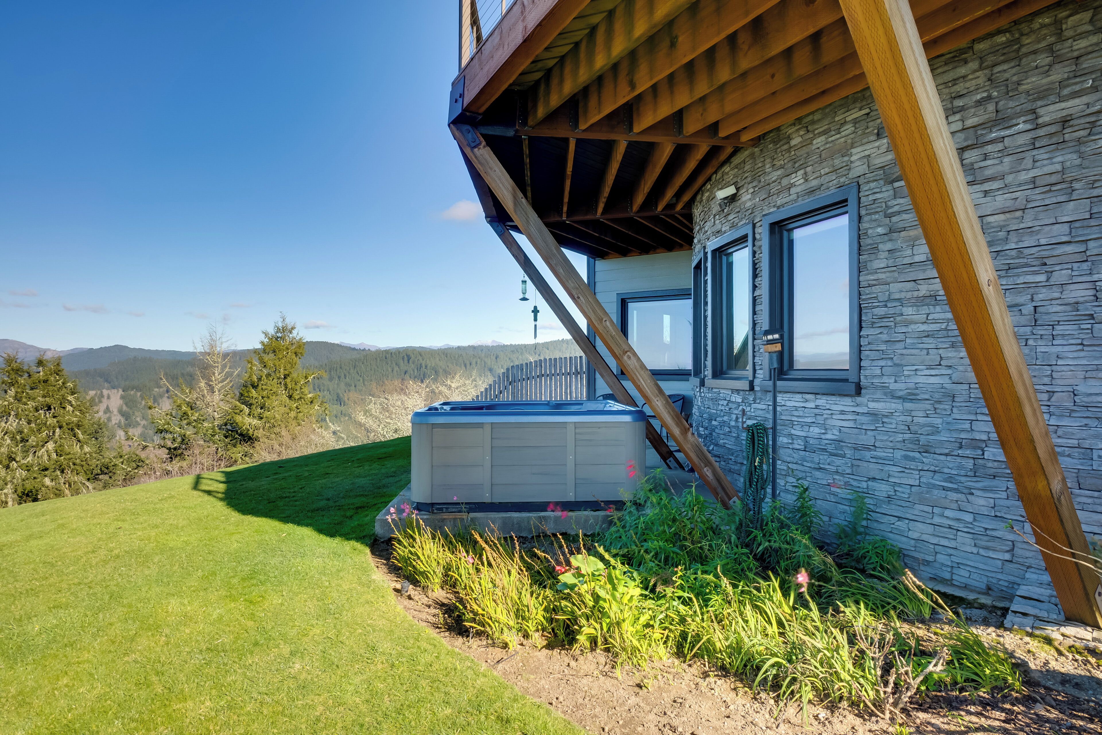 A modern house with a stone exterior, a wooden deck, and a hot tub in the yard.