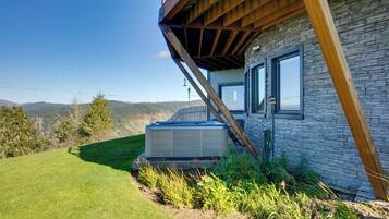 A modern house with a stone exterior, a wooden deck, and a hot tub in the yard.