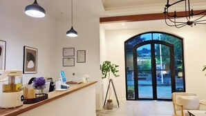 Un área de recepción moderna con mostrador de madera, iluminación colgante, certificados enmarcados y vistas a través de un amplio arco.