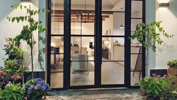 Una entrada moderna con puerta de cristal, plantas en macetas y un interior visible que incluye un comedor.