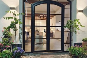 Une entrée moderne avec une porte en verre, des plantes en pot et un intérieur visible, comprenant un espace repas.
