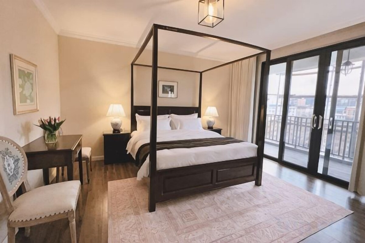 Un lit à baldaquin avec une table de chevet et une lampe, une chaise, et une vue sur l’extérieur grâce à une porte-fenêtre coulissante.
