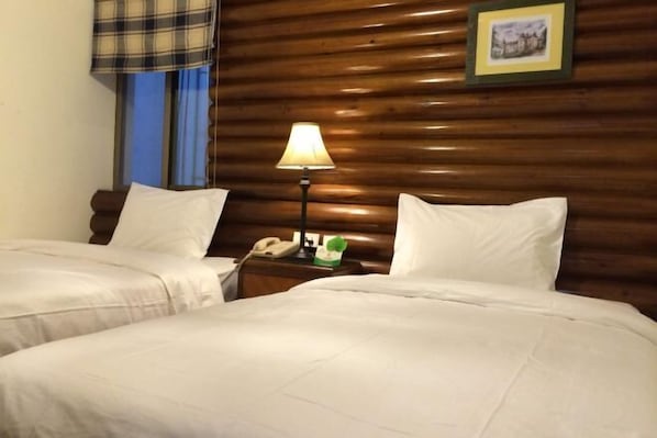 Ein Hotelzimmer mit zwei Betten, einem Holzkopfteil, einem Nachttisch mit Lampe, einem Telefon und einem gerahmten Bild an der Wand.