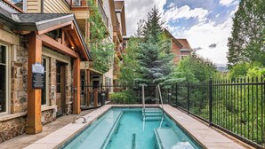 A swimming pool with stone walls, a wooden deck, and a metal fence.