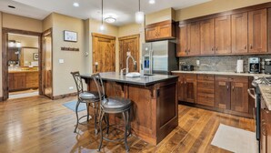 A kitchen with wooden cabinets, a stainless steel refrigerator, and a bar area with stools.