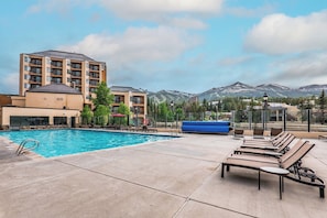 A pool area with lounge chairs, a building with multiple balconies, and a mountainous backdrop. - Luxe Breck Escape - 2BR & 2BA with Pool, Hot Tubs & Walk to Downtown (Breckenridge)