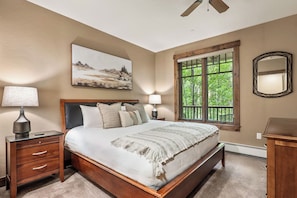 A bedroom with a bed, nightstands, a window with a view, and a ceiling fan. - Luxe Breck Escape - 2BR & 2BA with Pool, Hot Tubs & Walk to Downtown (Breckenridge)