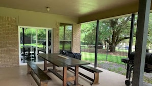 Un patio al aire libre con una mesa y bancos de madera, ventanas amplias y una parrilla.