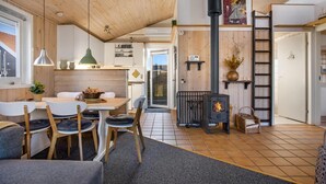 Interior acollidor d'una cabana amb zona de menjador, cuina, llar de foc i un dormitori en alt.