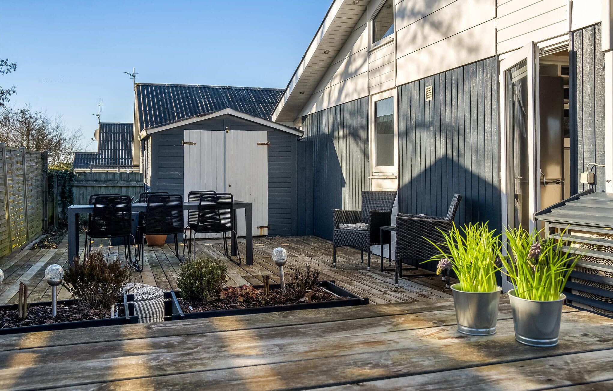 A patio with a table and chairs, a small shed, and potted plants.