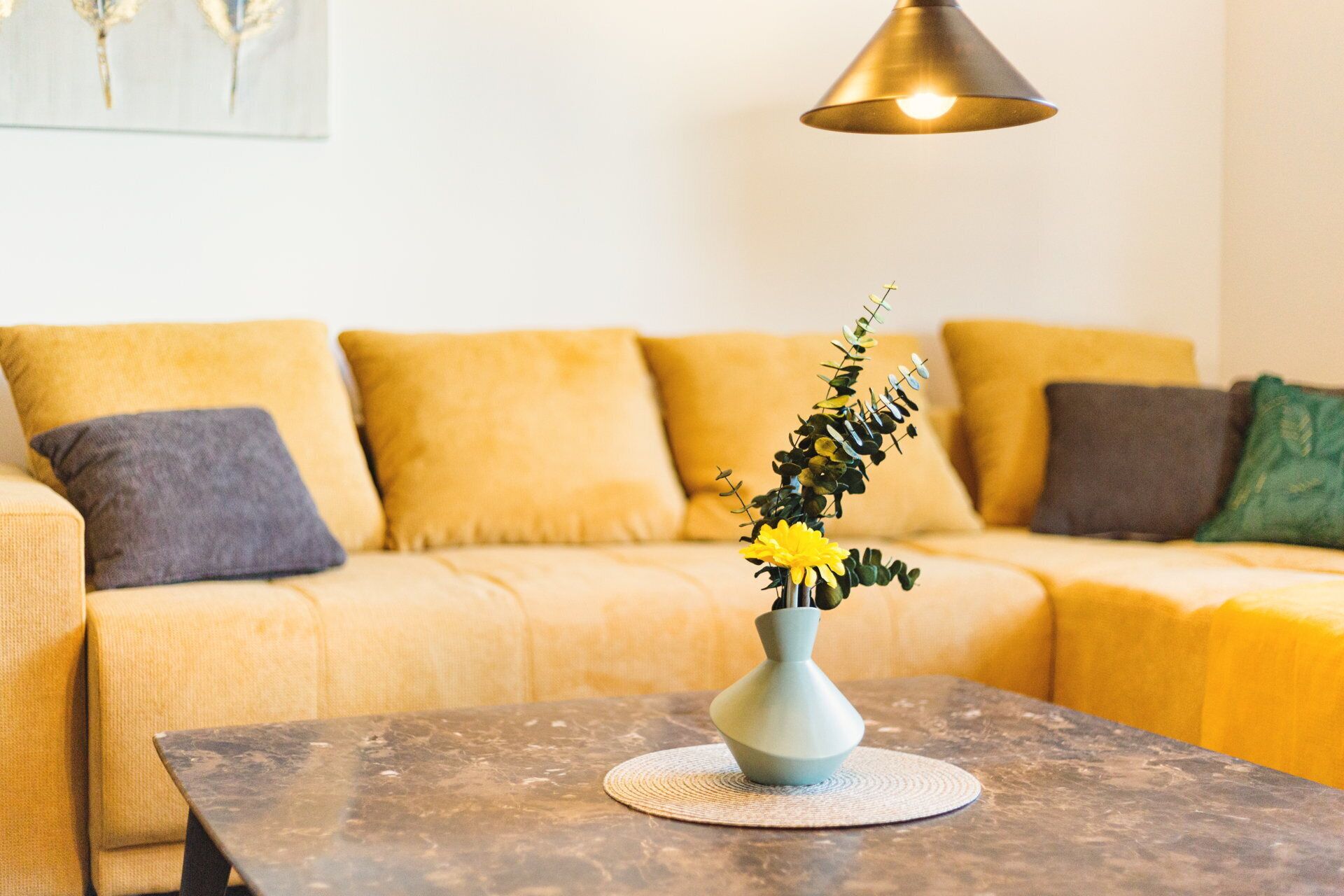 A living room with a sofa, a coffee table, and a vase with flowers.