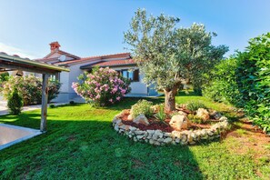 Enjoy a serene garden oasis with a large tree, flowering bush, and pergola structure.