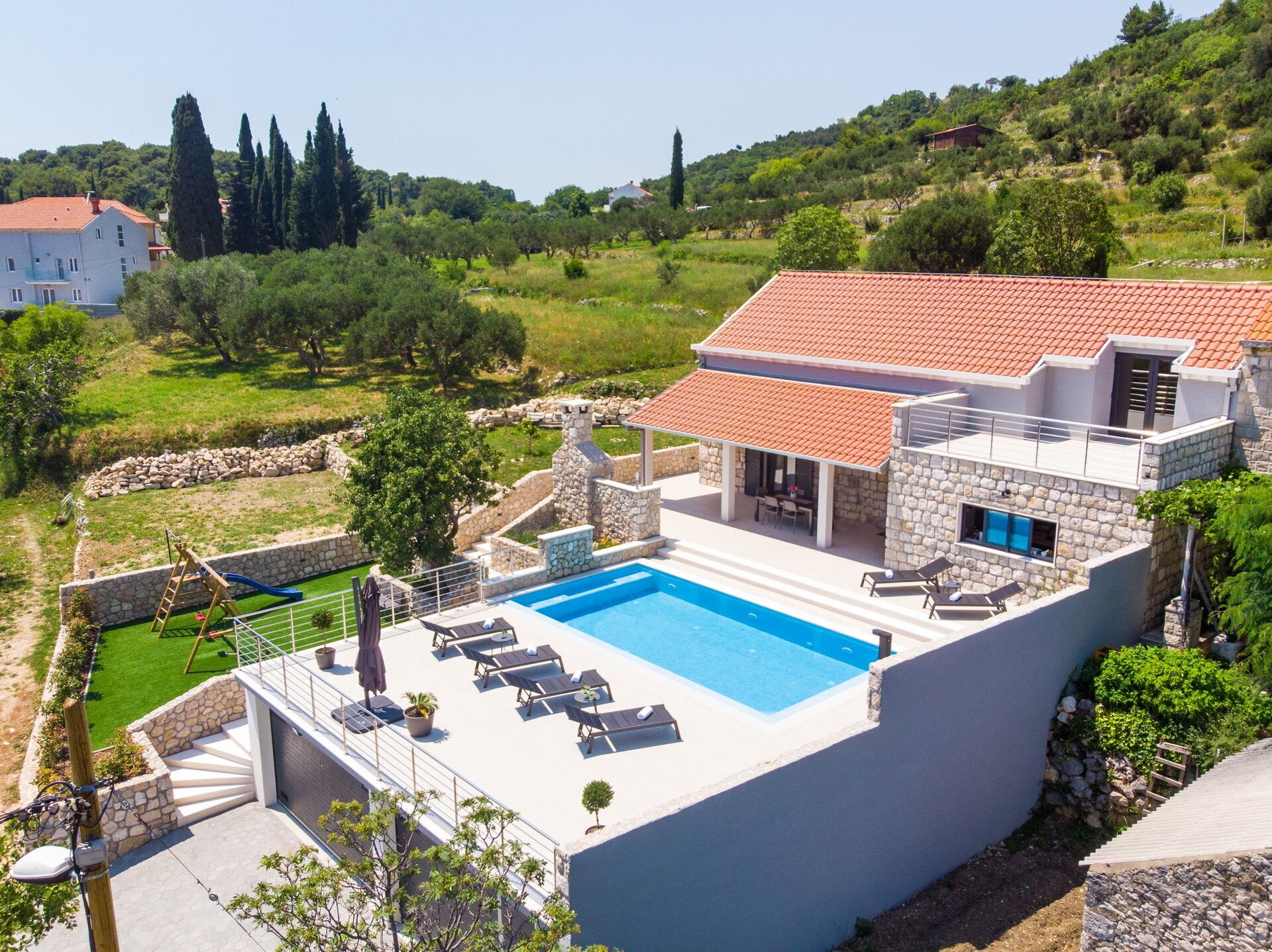 Eine moderne Villa mit Swimmingpool, Steinmauern und Blick auf die umliegende Landschaft.